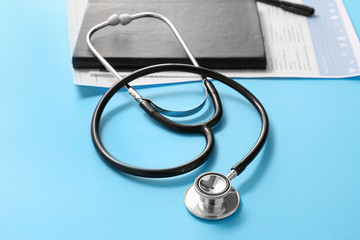Stethoscope, notebook and documents on color background. Cardiology concept
