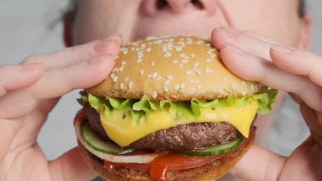 Woman eating tasty beef burger with cheese and golden bun closeup.