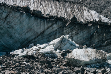 Natural texture of big glacial wall with crevasses close-up. Atmospheric nature background with ice boulders near icy broken wall with cracks. Big peace of ice and stones near surface of glacier.