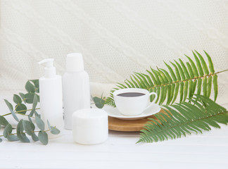 Spa composition of Jar of cream and shampoo bottle with black coffee cup on bamboo plate over decoration background of green fern and eucalyptus.