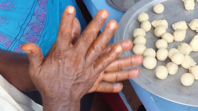 Indian dinner party preparations: Close up of Indian hands rolling Indian sweet rasgulla dough into small balls on a large metal plate to be boiled in sugar syrup