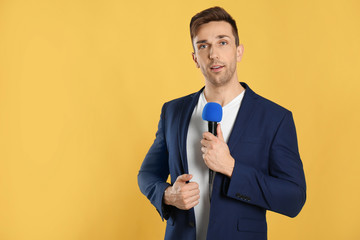 Young male journalist with microphone on yellow background. Space for text