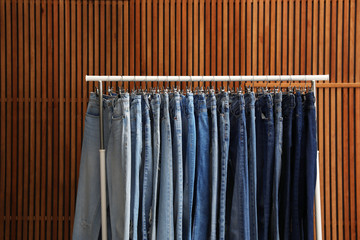 Rack with different jeans on wooden background