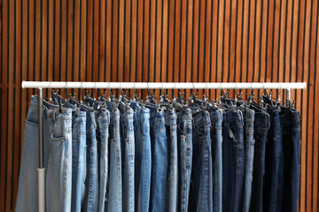 Rack with different jeans on wooden background