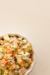 Olivier in a white plate on a pale pink background. the winter salad.ingredients: cucumber, sausage, meat, mayonnaise, sour cream, potatoes, peas, egg. space for your text.