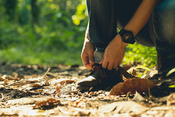 Young traveler hiker tying shoelace on trail in grassland.Tourist tie his boots.Tourism concept