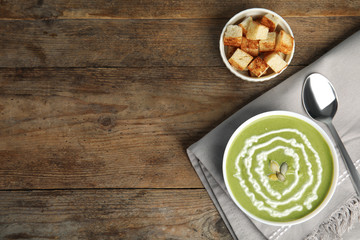 Delicious broccoli cream soup served on wooden table, flat lay. Space for text