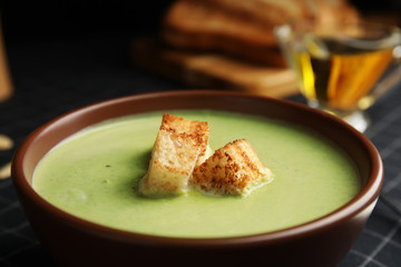 Bowl of delicious broccoli cream soup with croutons on table, closeup