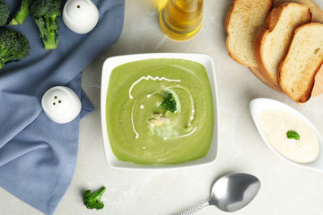 Delicious broccoli cream soup served on grey marble table, flat lay