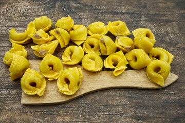 Detail of raw Tortellini, traditional italian pasta, on a woodem spoon. Wooden background. Macro image.
