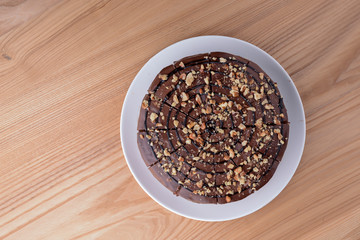 Sweet chocolate spider web cake with frosting on top served on a white plate on light wooden background.