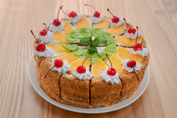 Sweet summer fruit cake with slices of orange, kiwi, cherries. frosting and whipped cream on top