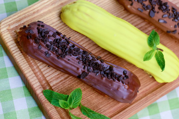 Traditional french dessert eclair pastry, three pieces laying on wooden board on a table covered...