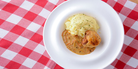 Traditional cuisine, mashed potatoes with gravy, meat and dill served on a white plate on a plaid background