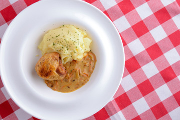 Traditional cuisine, mashed potatoes with gravy, meat and dill served on a white plate on a plaid background