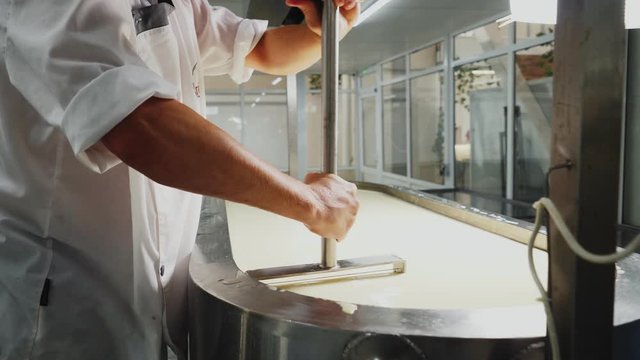 worker mixes raw cheese in large reservoir at plant closeup