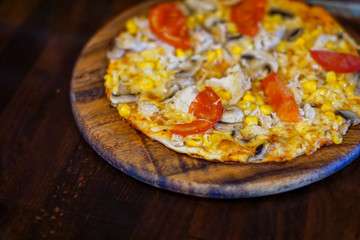 Delicious fresh pizza with meat, tomatoes and mushrooms served on a board on dark wooden table, close up