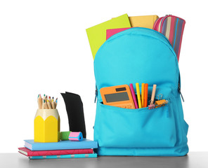 Bright backpack with school stationery on grey stone table against white background