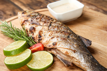 Delicious grilled fish with lime on wooden board, closeup