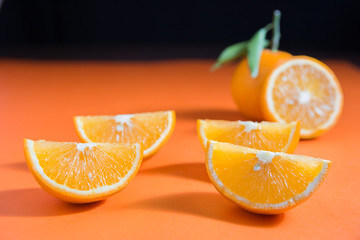 orange cut into four pieces with a full orange and half cut orange in the background on orange...