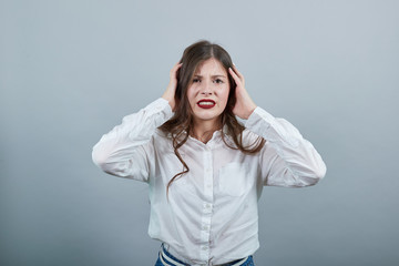 Confused caucasian young woman in fashion white shirt holding hands on head with opened mouth, looking at camera isolated on gray background in studio. People sincere emotions, lifestyle concept.