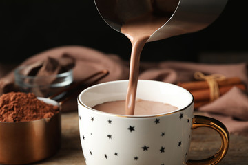 Pouring hot cocoa drink into cup on wooden table