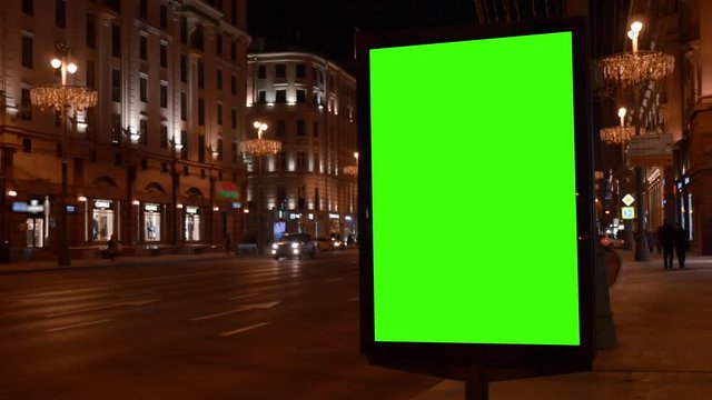 Winter evening. City street. close city light vitrine with empty green screen on roadside against cars driving along night Background blurred Close-up