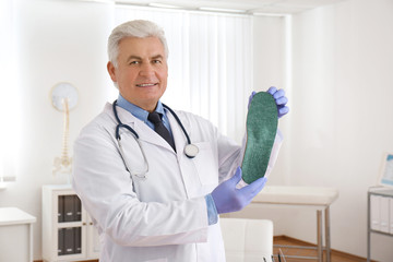 Senior male orthopedist showing insole in clinic