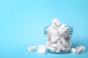 Glass jar full of rolled paper sheets on light blue background, space for text