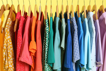 Bright clothes on hangers against yellow background, closeup. Rainbow colors
