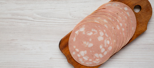 Sliced Mortadella Bologna Meat on a rustic wooden board over white wooden surface, view from above....