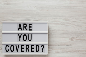 'Are you covered?' words on a modern board on a white wooden surface, top view. Overhead, from above, flat lay. Space for text.
