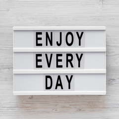 'Enjoy every day' words on a modern board on a white wooden surface, top view. Overhead, from above, flat lay. Close-up.