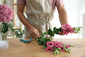 Obraz na płótnie Canvas Florist making beautiful bouquet at table in workshop, closeup