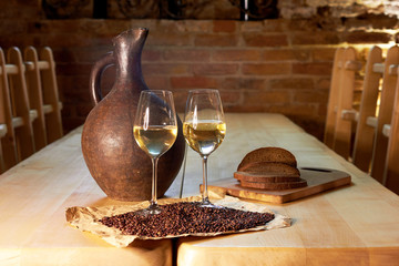 Two glasses of white wine, grape seeds, a clay jug and a few pieces of bread on a wooden table in a restaurant