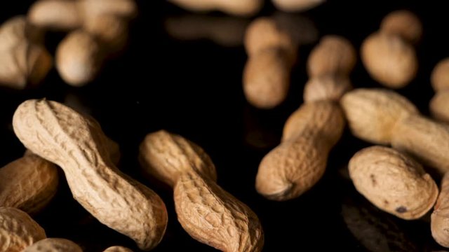 Bunch of peanuts drop from above onto black table. Closeup static studio shot.