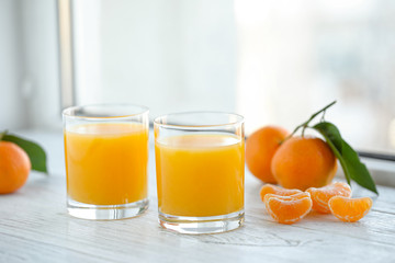 Glasses of fresh tangerine juice and fruits on white wooden table