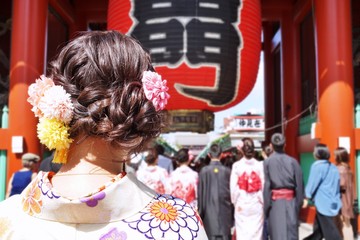 A woman in a Kimono looking towards the kaminarimon gate of Sensoji temple in Asakusa, Tokyo, Japan. The Japanese words means Kaminarimon or Kaminari gate.