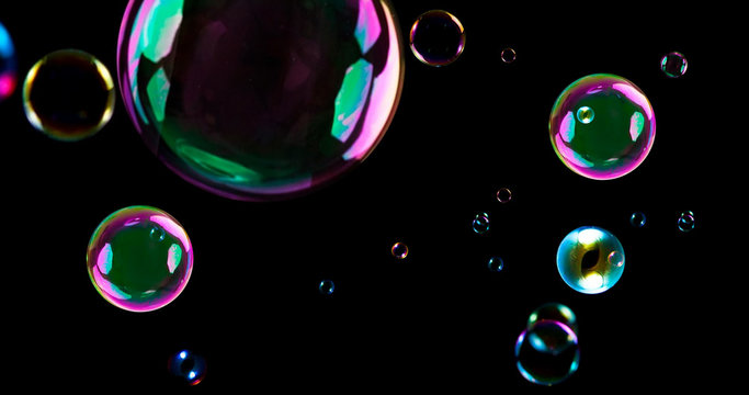 Floating colorful soap bubbles with iridescent reflection isolated on black background, abstract water spheres