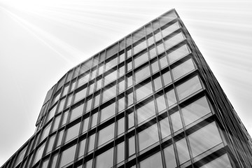 Fototapeta na wymiar Sun rays light effects on urban buildings in sunset. Modern office building detail, glass surface with sunlight. Business background. Black and white.
