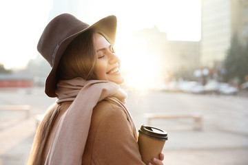 Young woman with cup of coffee on city street in morning
