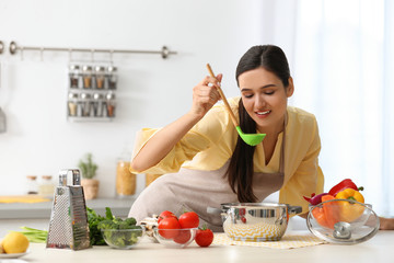 Young woman tasting delicious soup in kitchen