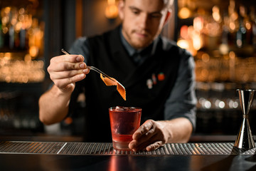 Bartender putting slice of orange rind in cocktail