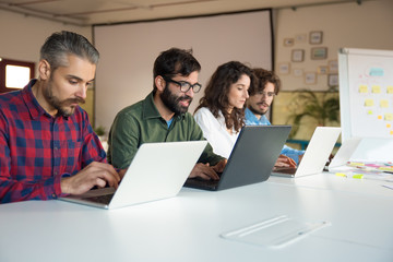 Startup team collaborating on project, using laptops at conference table. Business colleagues in casual working together in contemporary office space. Teamwork concept