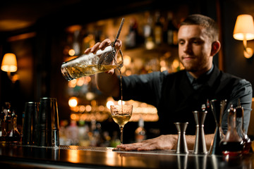 Bartender with facial hair pours drink with strainer