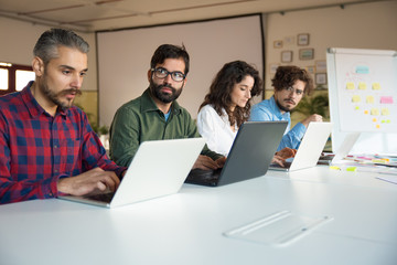Line of coworkers sitting at conference table, using laptops in meeting room. Business colleagues in casual working together in contemporary office space. Startup team concept