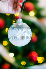 Naklejka premium Christmas, decoration, holidays and people concept - close up of woman hand holding christmas ball over living room and tree background