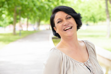 Cheerful young woman laughing outdoors. Portrait of beautiful happy middle aged woman standing and smiling in park. Emotion concept