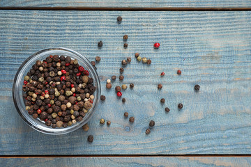 Mixed peppercorns in jar on blue wooden table, flat lay
