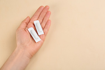 Closeup view of woman holding suppositories on beige background, space for text. Hemorrhoid...